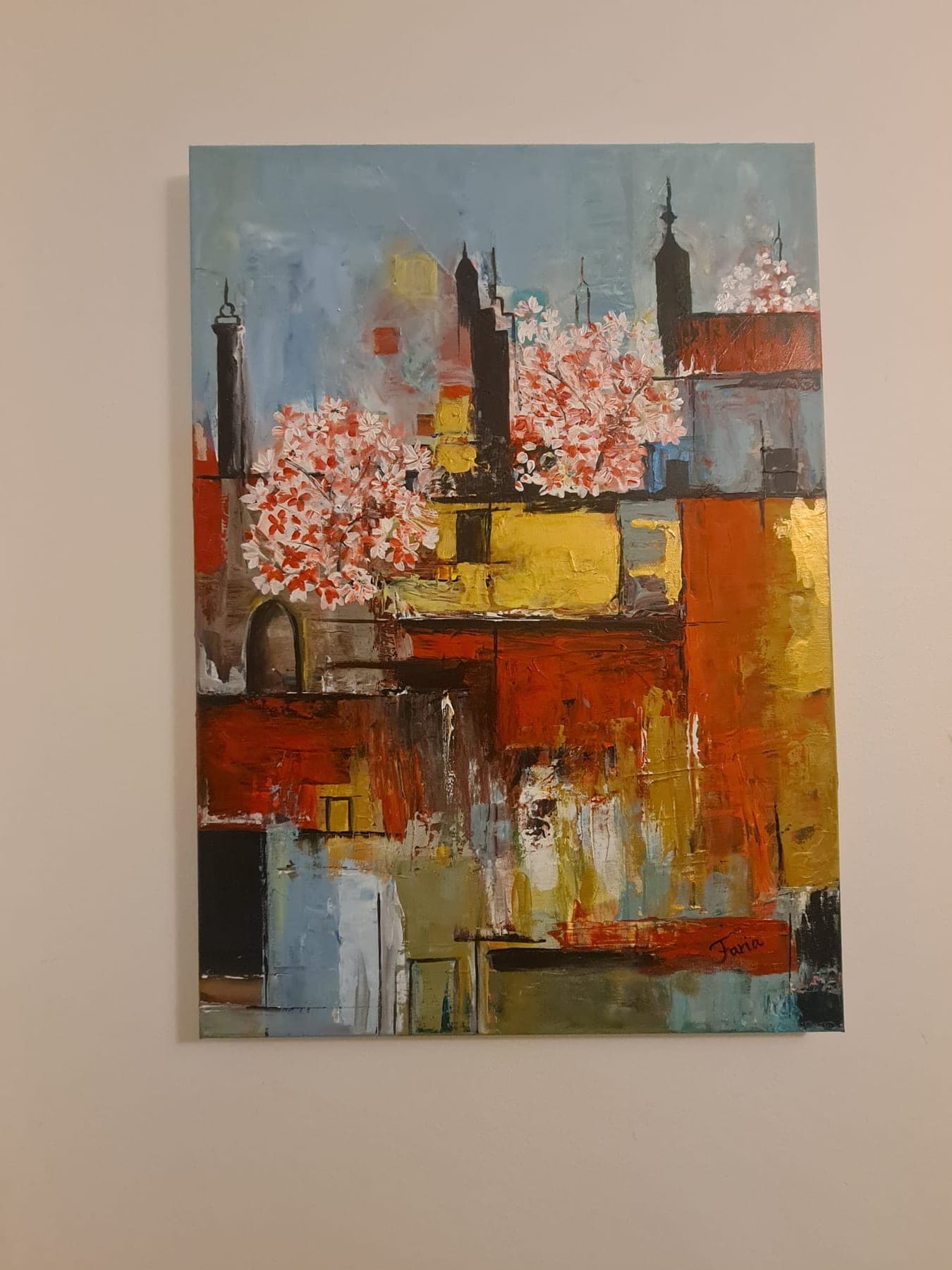 A mounted abstract of rust, ochre and pale grey blocks suggesting rooftops and towers, with pink blossom breaking across the upper half.