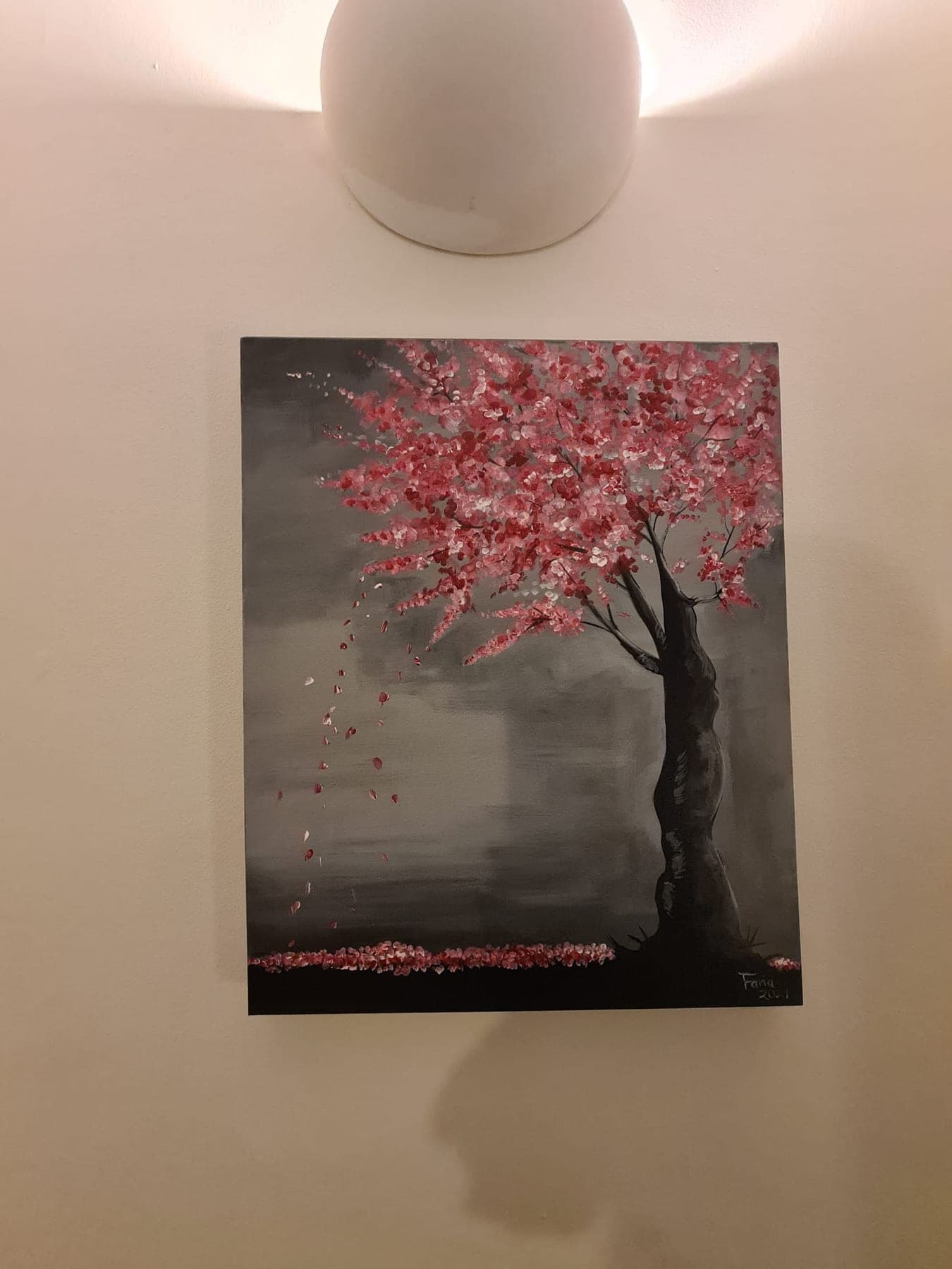 A grey, misted ground with a dark leaning trunk carrying a heavy canopy of red and pink blossom, petals falling to the ground below.