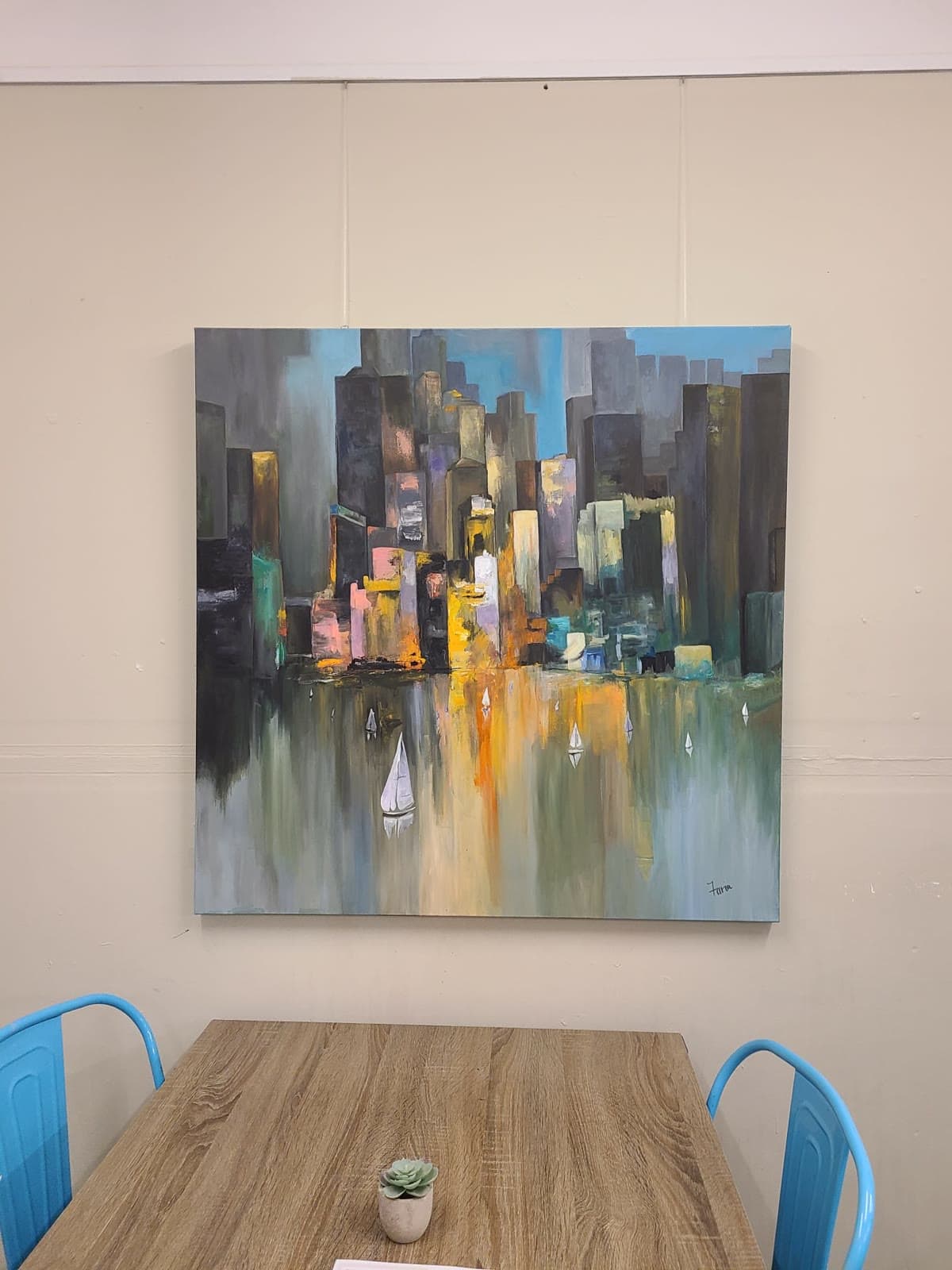 Large square acrylic canvas of a city skyline in greys, teals and ochre, dissolving into its own reflection, with small white sailing boats on the water below.