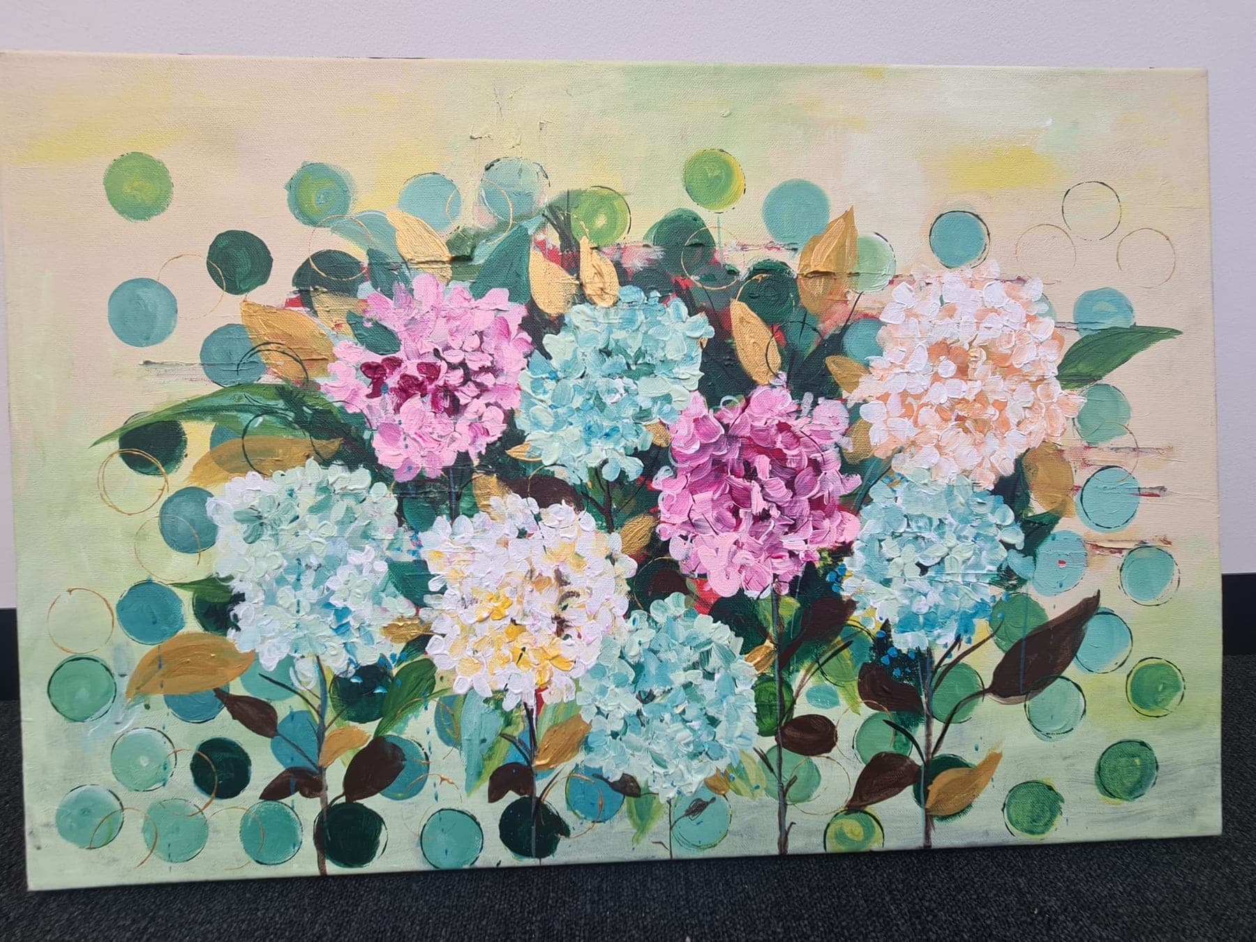 Pink and pale blue hydrangea heads with copper and green leaves, set against a soft ground patterned with flat teal circles.